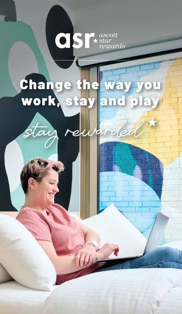 A person sits on a bed with a laptop, set against a colorful, modern interior design backdrop.