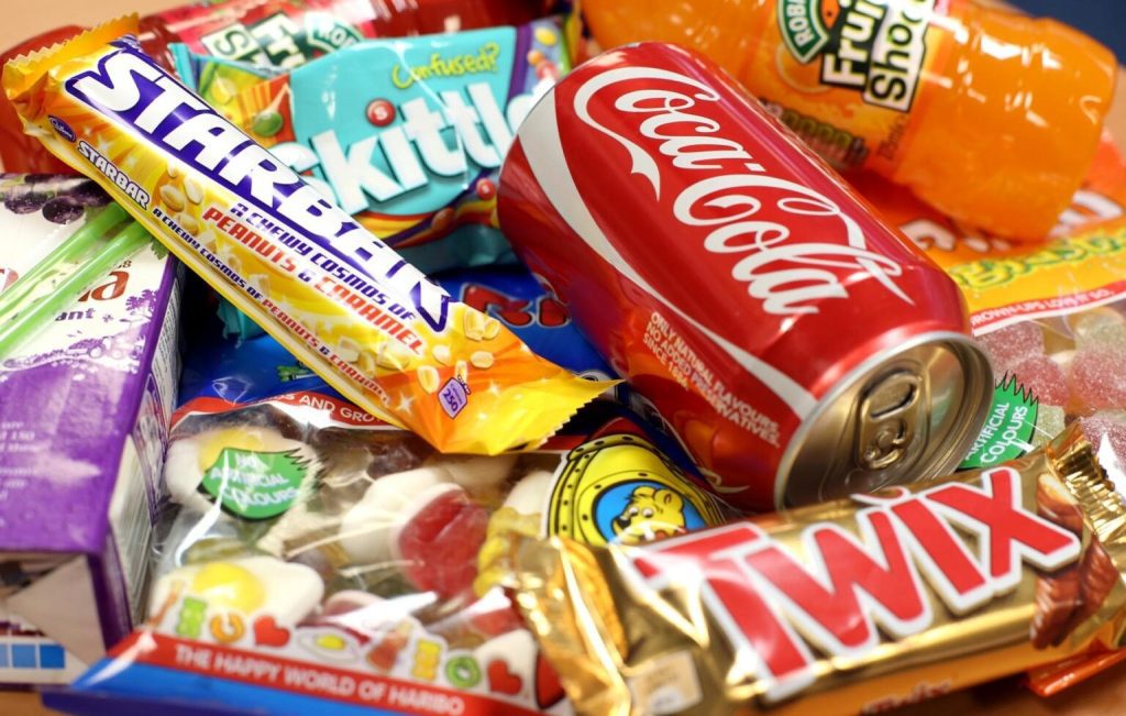 Assorted candies, snacks, and beverages, including Coca-Cola, Twix, Skittles, and Haribo gummies.
