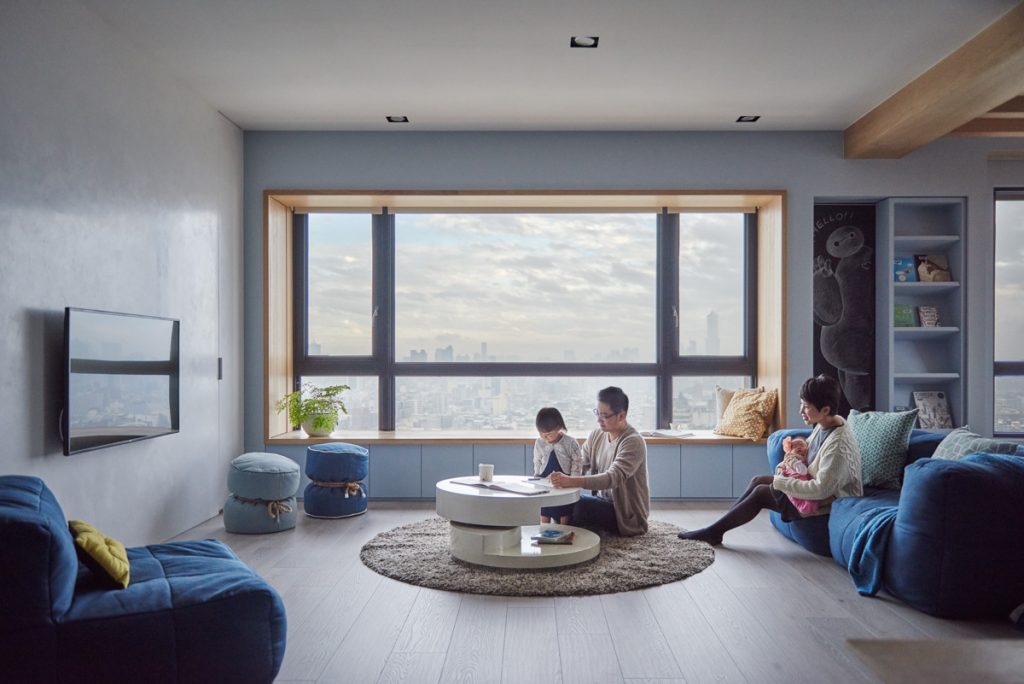A modern living room with large windows, cozy seating, and a family engaging in activities together.