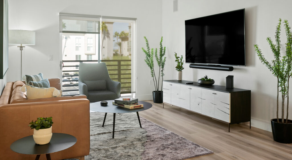 Modern living room with sleek furniture, neutral tones, large TV, and indoor plants.
