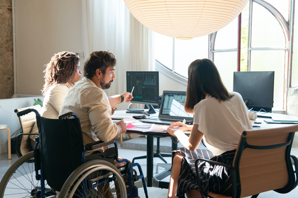 Three colleagues collaborate in a modern office, with one using a wheelchair for mobility.