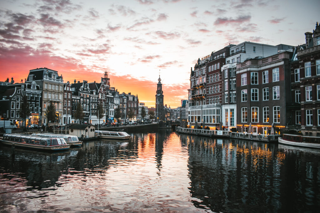 A serene canal in Amsterdam at sunset, lined with historic buildings and illuminated boats.