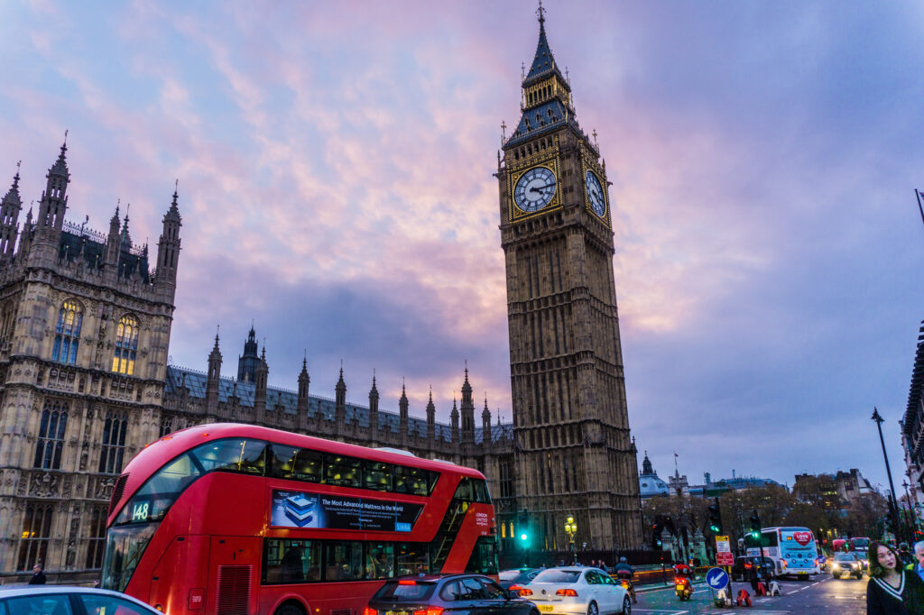 Big Ben and the Houses of Parliament tower over a busy London street with iconic red buses.