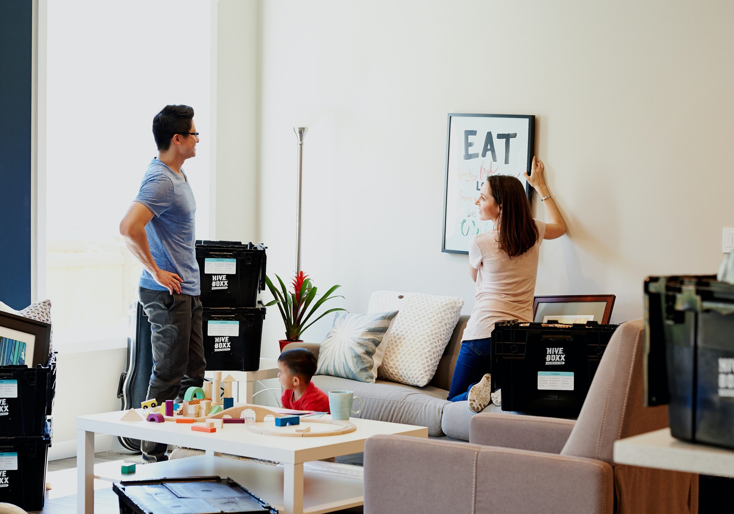 A family arranges decor in a living room surrounded by moving boxes and children's toys.