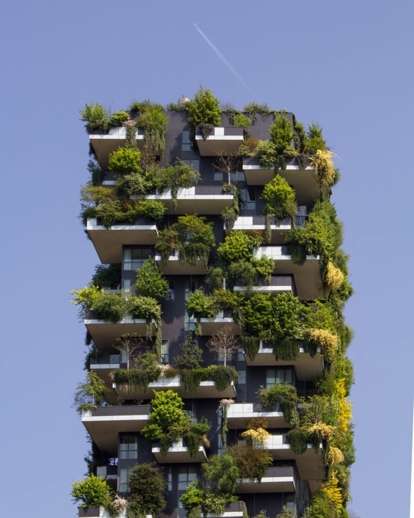 A modern high-rise building features lush greenery integrated into its balconies and facade.