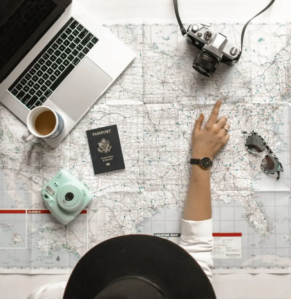 Travel planning essentials on a map, including a laptop, camera, passport, and coffee.