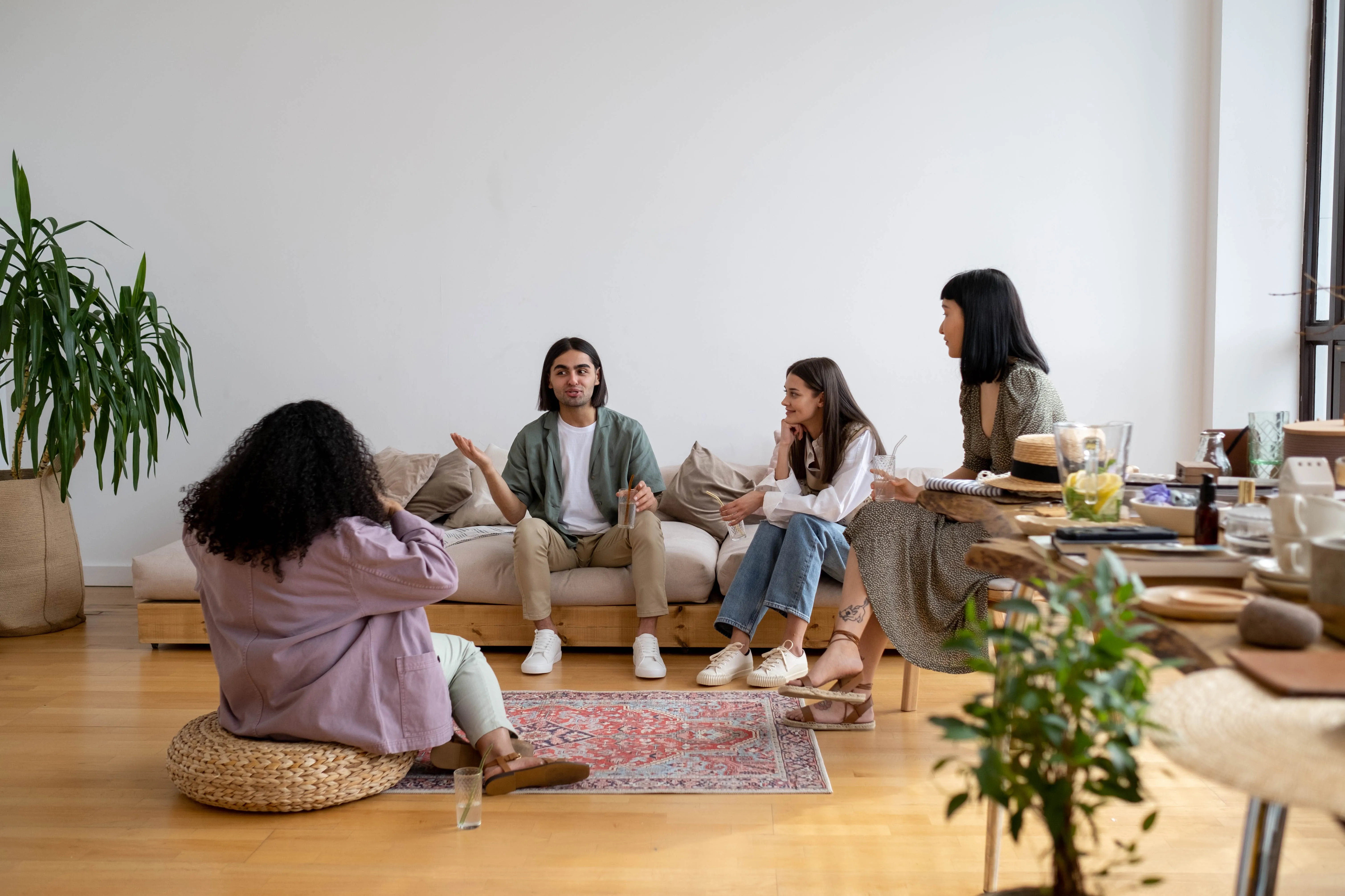 A casual indoor gathering with four people seated, surrounded by decor and natural light.