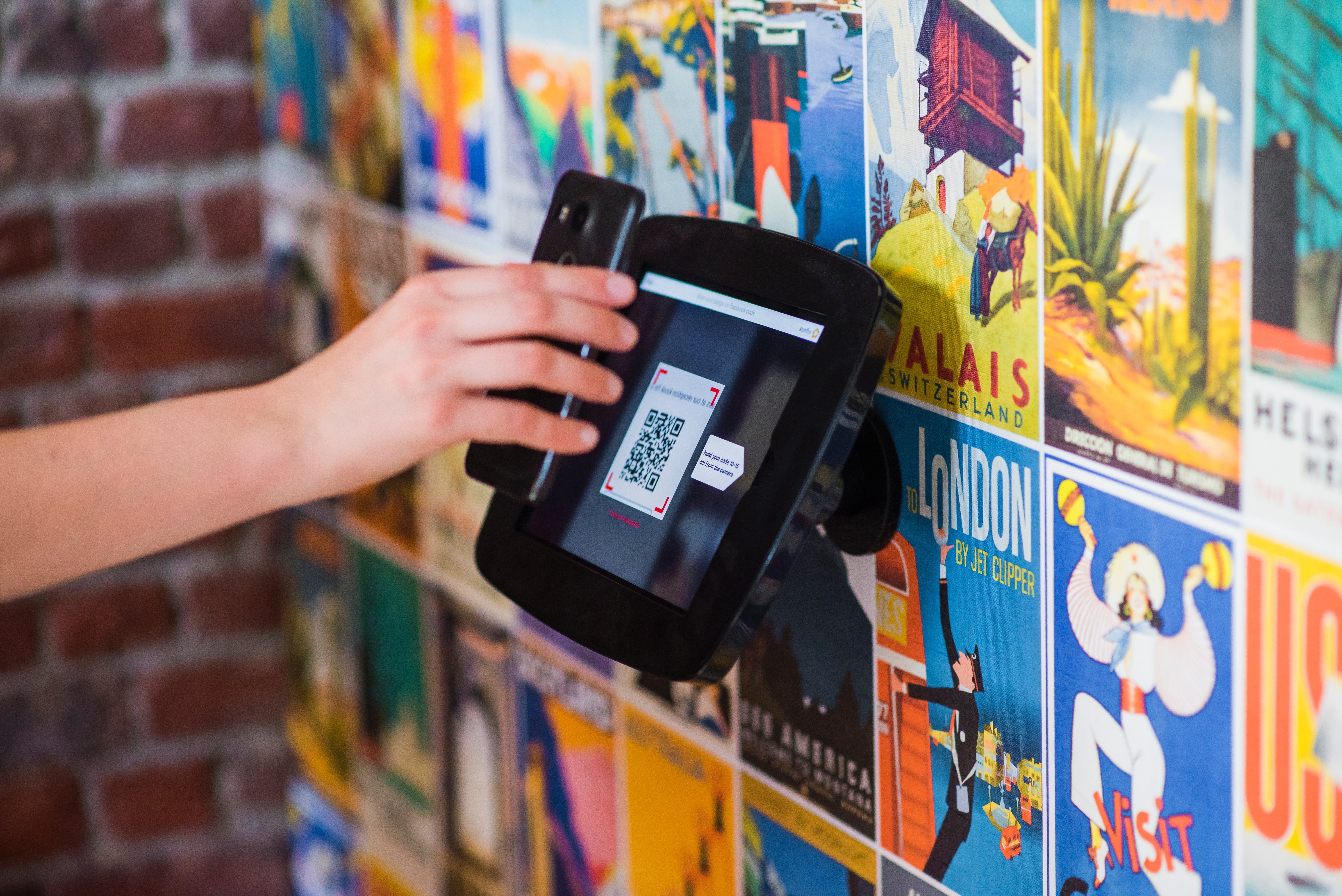 A person scans a QR code on a tablet against a colorful vintage travel poster background.