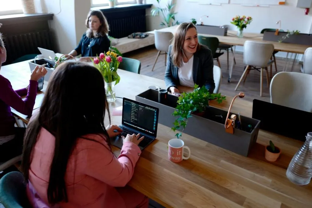 A modern coworking space with individuals working on laptops, surrounded by plants and decor.