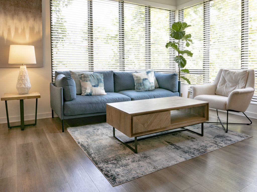 Modern living room with a blue sofa, neutral decor, and large windows with blinds.