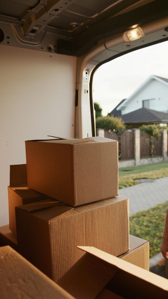 Cardboard boxes stacked inside a van, with a suburban house visible in the background.