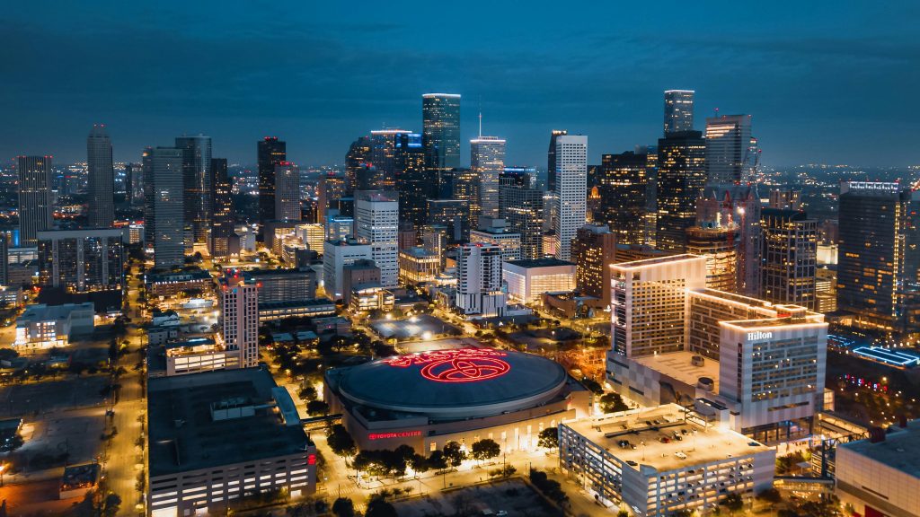 A vibrant nighttime view of downtown Houston, featuring the Toyota Center and illuminated skyscrapers.