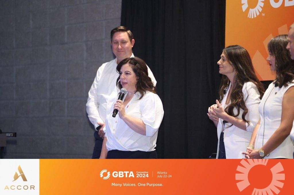 Individuals in business attire speak on stage at the GBTA 2024 event in Atlanta, hosted by Accor.