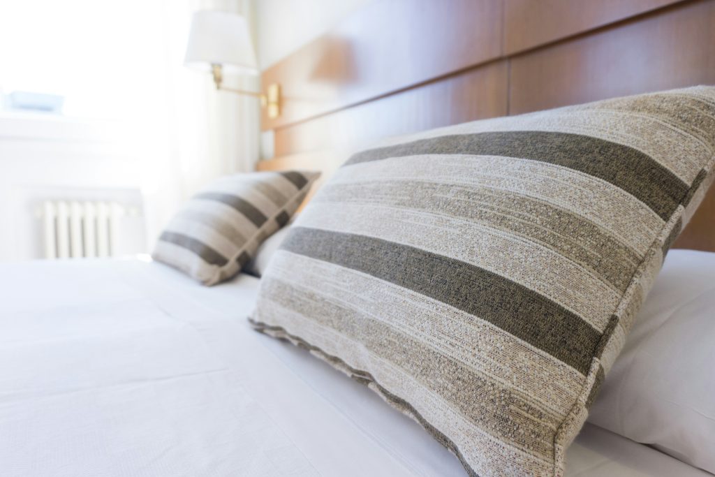 Striped pillows rest on a neatly made bed with a wooden headboard and soft natural lighting.