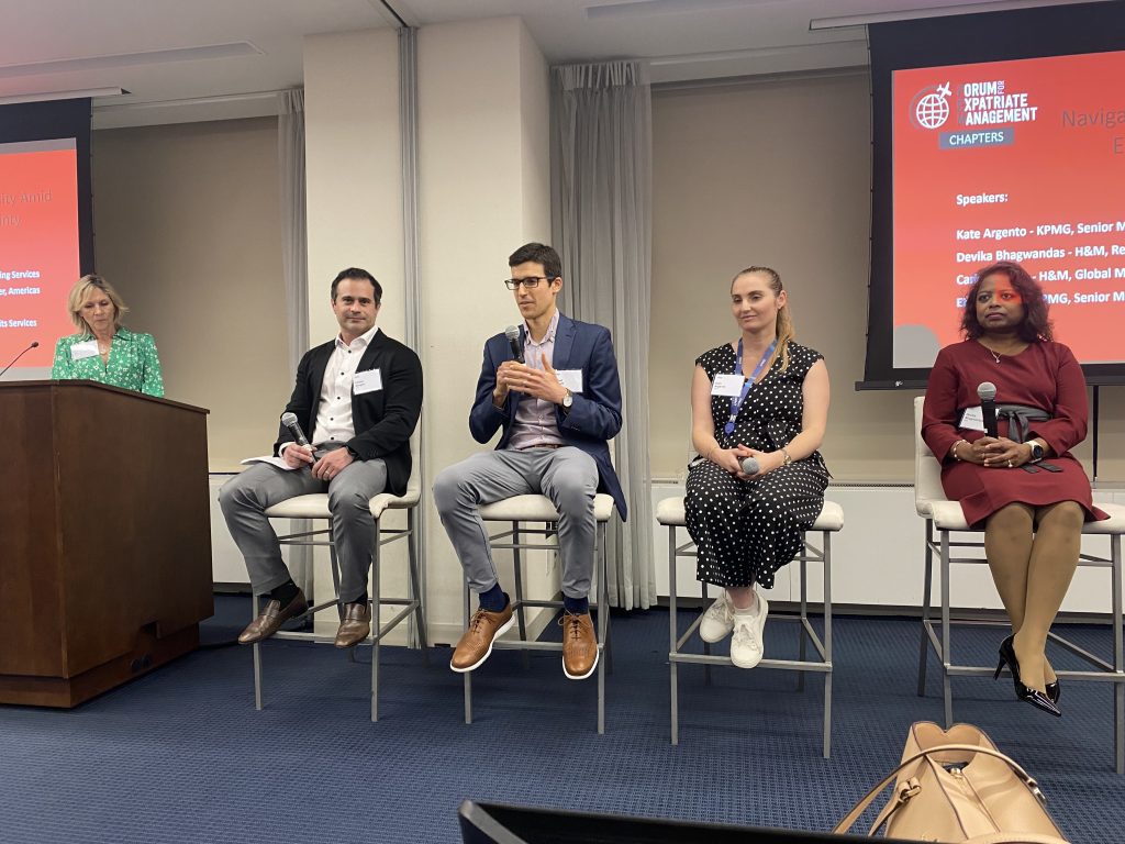 A panel discussion with speakers seated on stools, accompanied by a presenter at a podium.