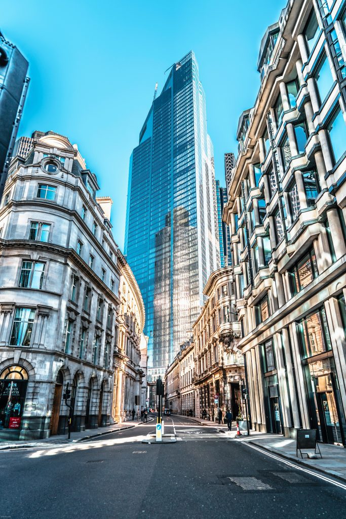 Modern skyscraper towers over historic architecture on a bright, clear city street.