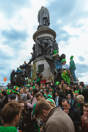 A festive crowd dressed in green gathers around a monument, celebrating St. Patrick's Day.