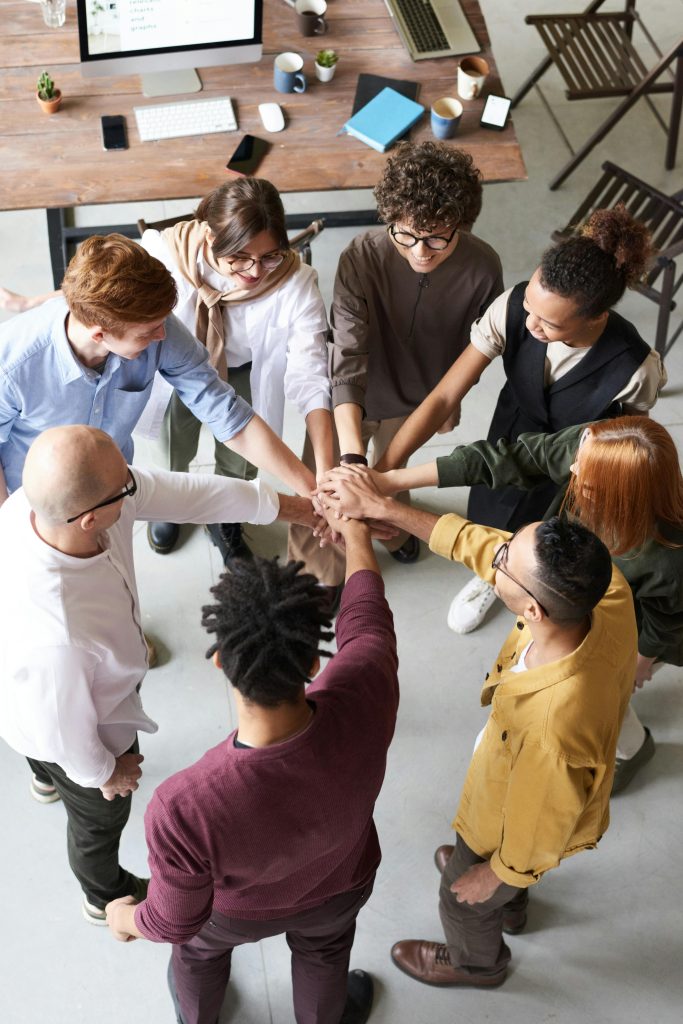 A diverse group of people stands in a circle, joining hands in a collaborative team gesture.