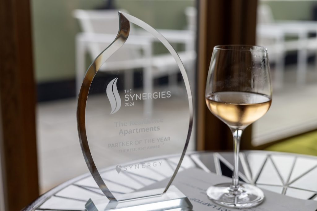 An elegant award trophy beside a glass of rosé wine on a reflective table.
