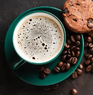 A cup of coffee next to a cookie on a plate.
