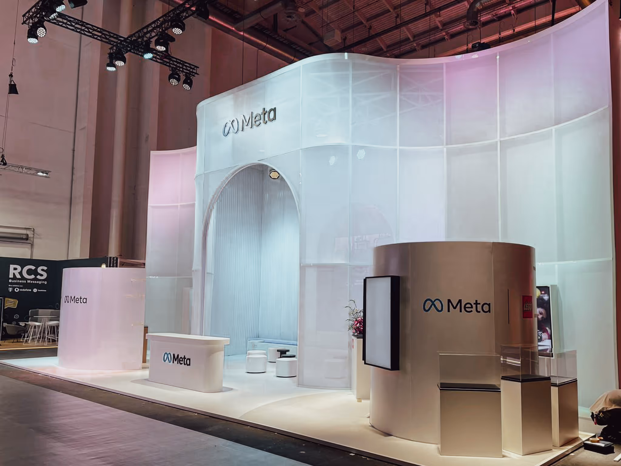 Moderner Messestand von Meta mit hellen, geschwungenen Wänden, Sitzbereichen und beleuchteten Werbeflächen.