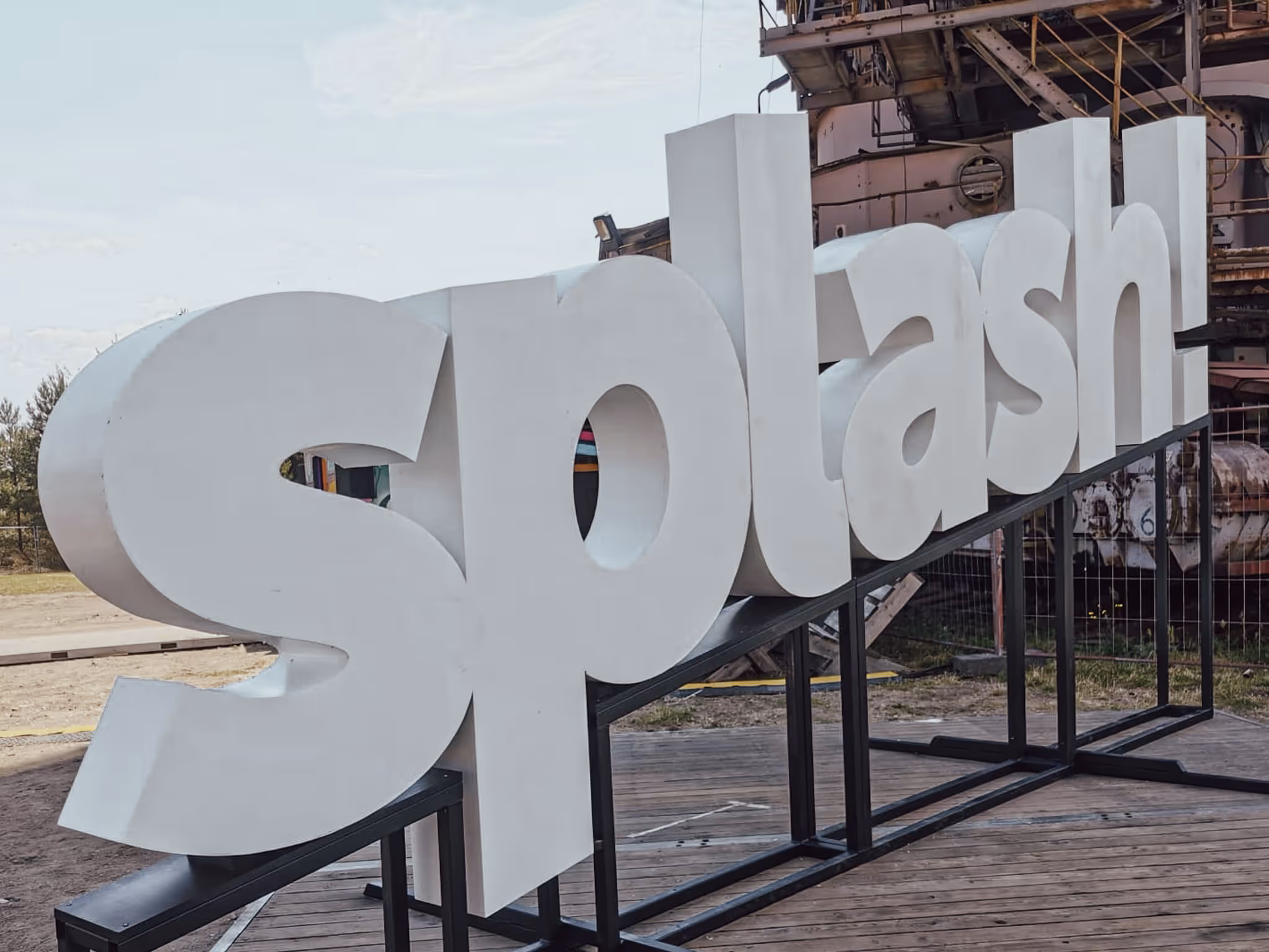 Große weiße 3D-Buchstaben bilden das Wort ‚Splash!‘ auf einer Metallstruktur im Freien.
