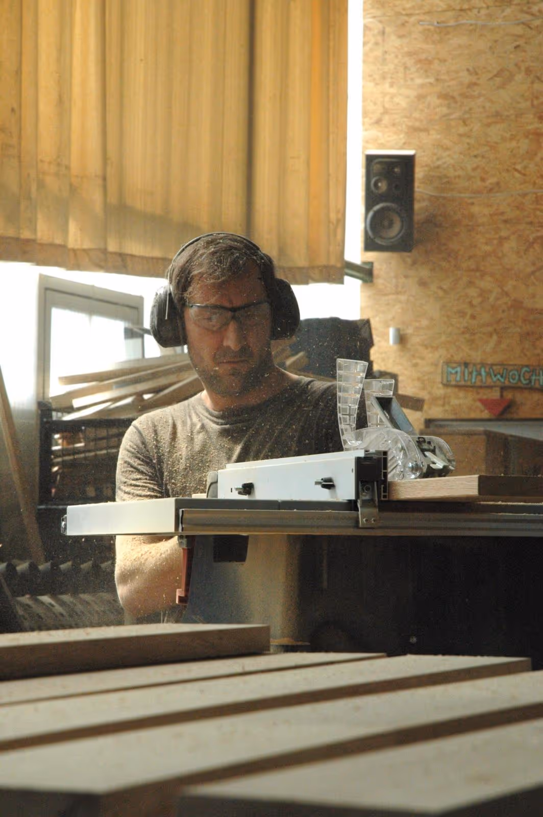 Ein Mann mit Gehörschutz und Schutzbrille arbeitet an einer Holzbearbeitungsmaschine in einer Werkstatt.