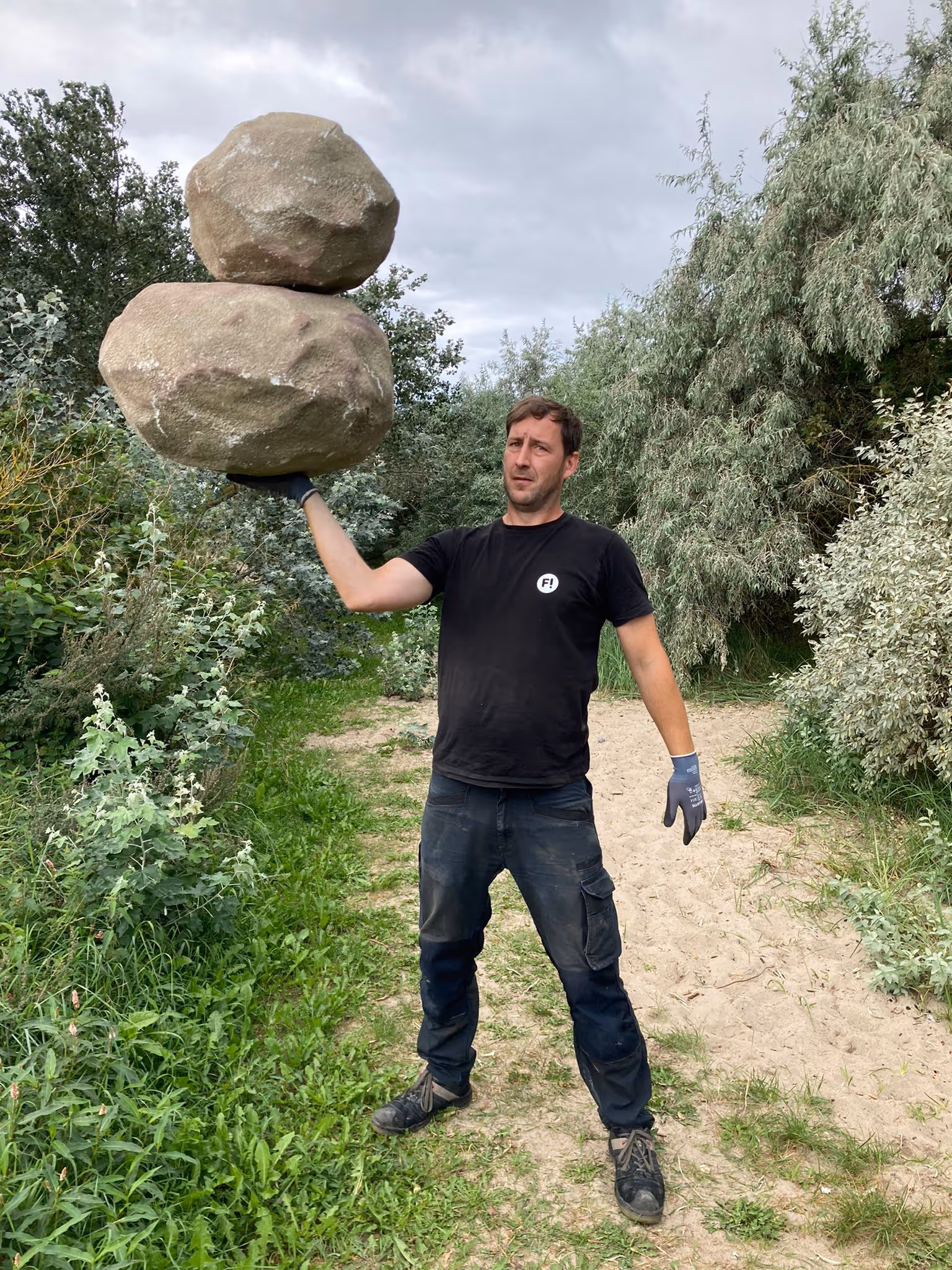 Mann steht im Freien und balanciert mit einer Hand zwei große Felsen aufeinander.
