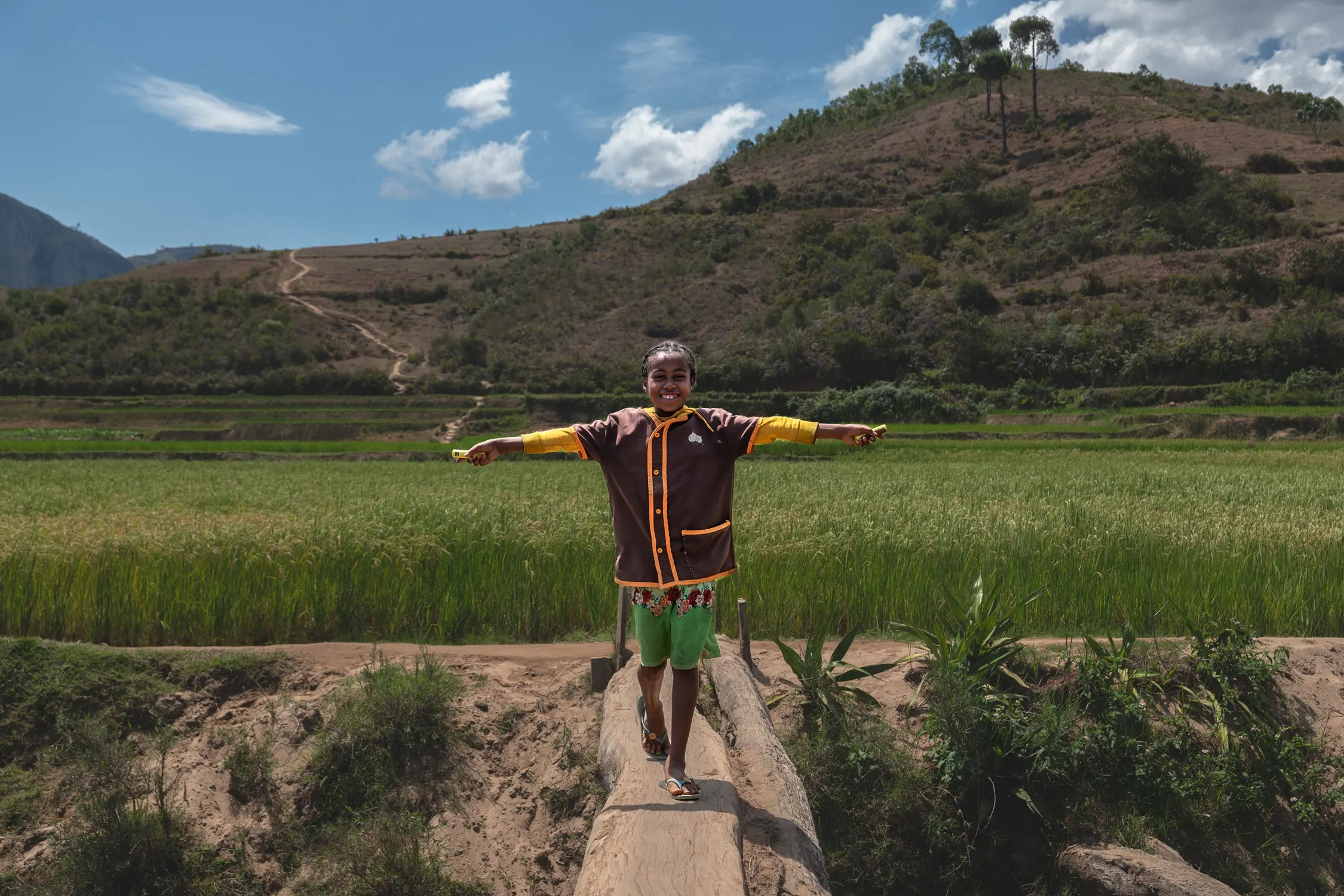 A girl standing on the wooden beam with arms spread holding two solar batteries.