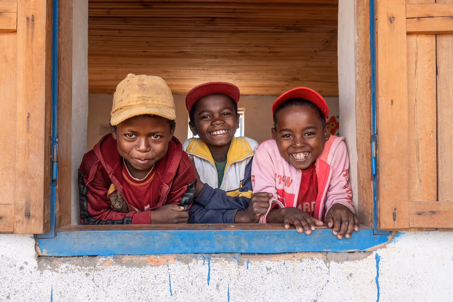 Three children leaning on the window frame and smiling. 