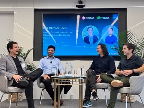 Four panelists seated on a stage, chatting and smiling around a glass-topped table.