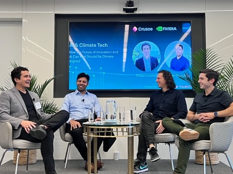 Four panelists seated on a stage, chatting and smiling around a glass-topped table.