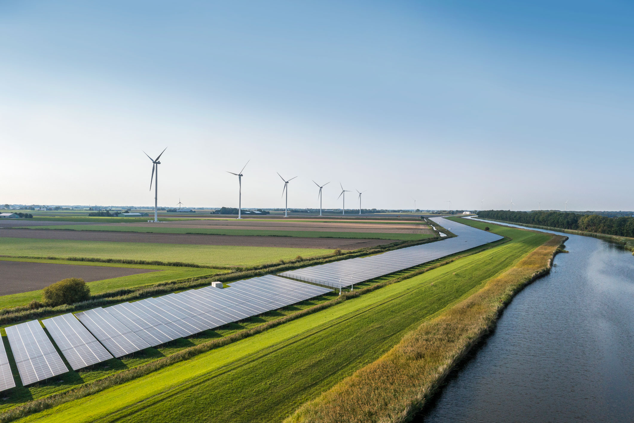 Rows of solar panels next to a canal with wind turbines on the horizon, illustrating sources powering Crusoe’s data centers.