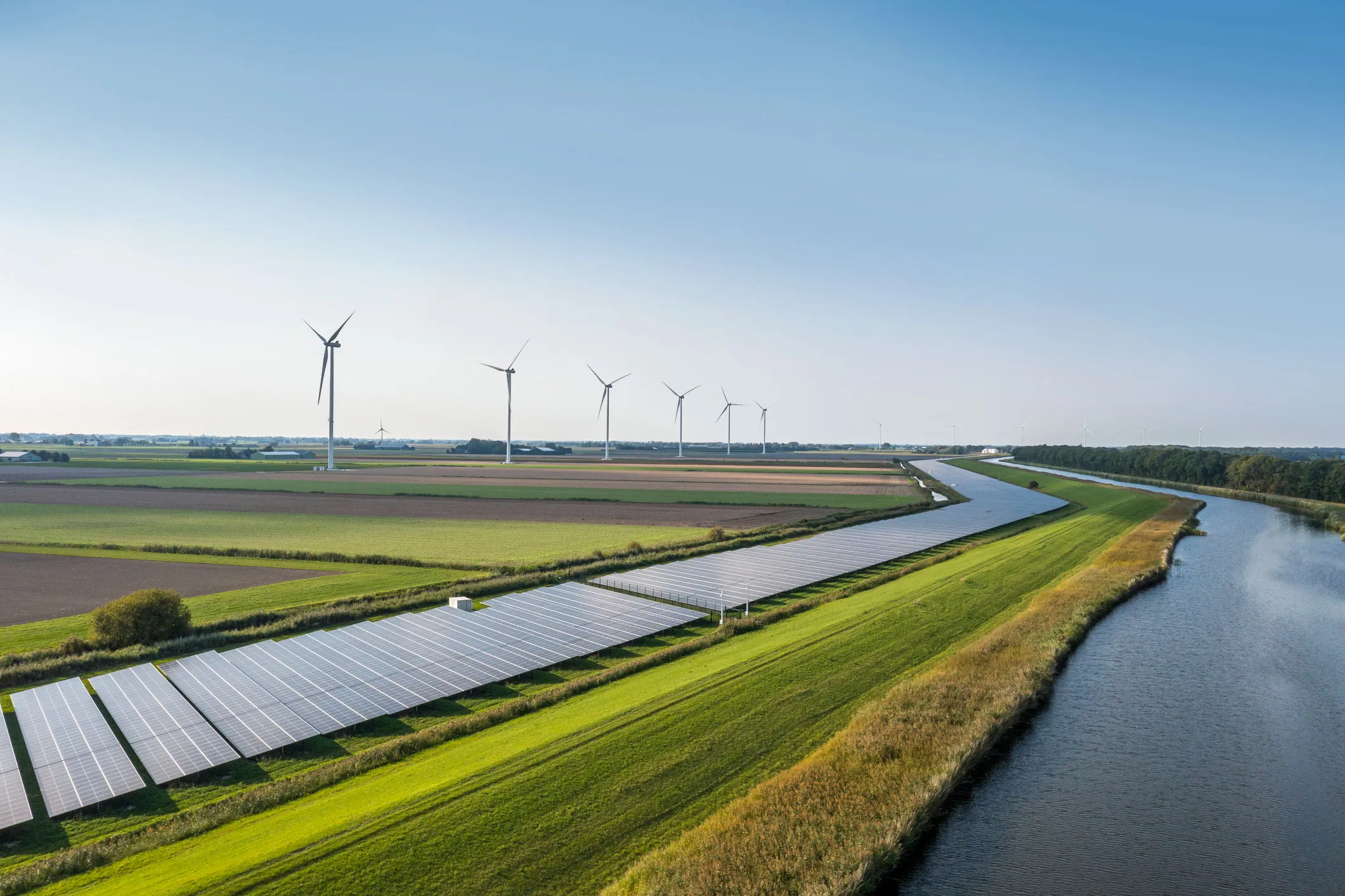 Rows of solar panels next to a canal with wind turbines on the horizon, illustrating sources powering Crusoe’s data centers.