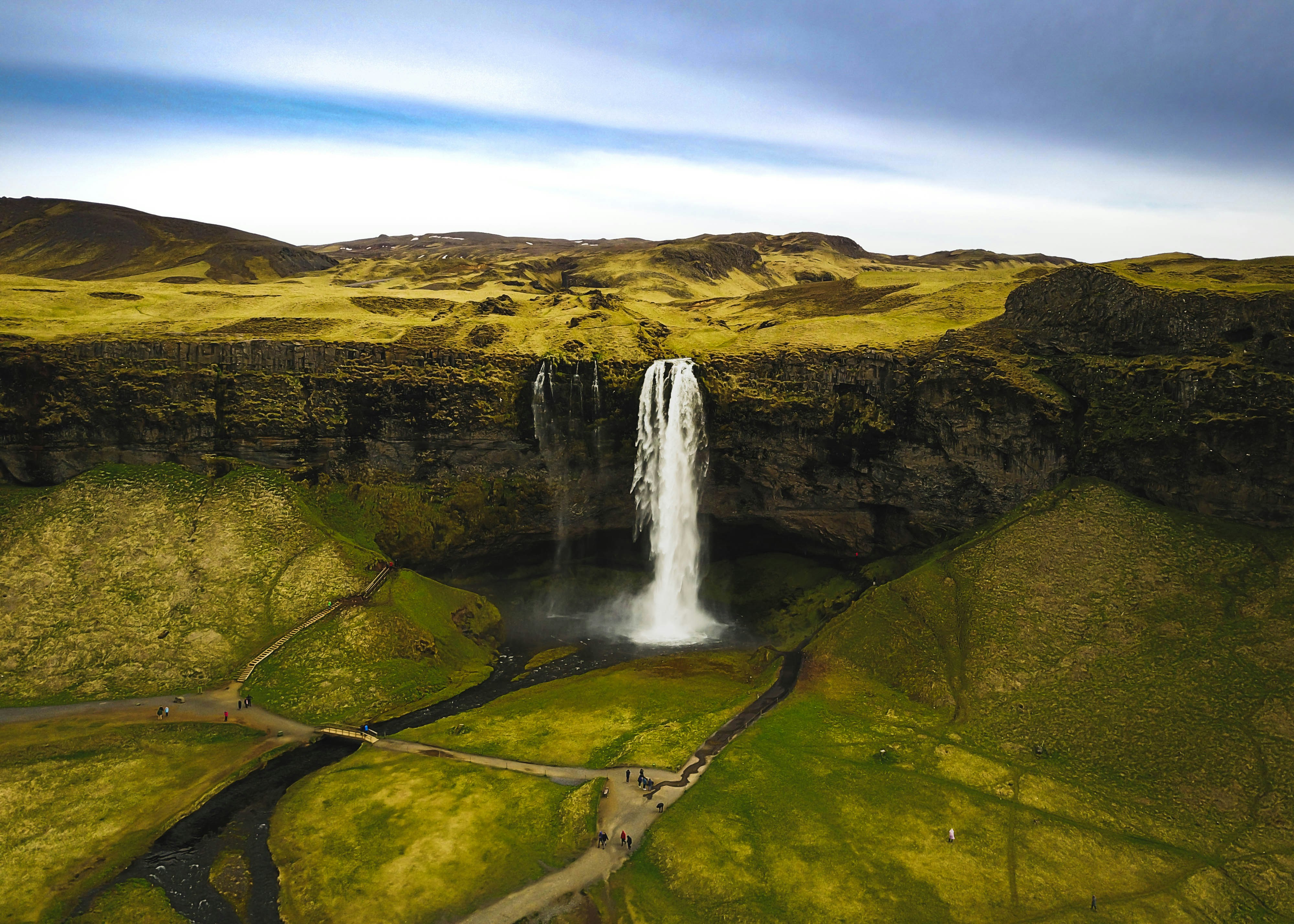 Aerial view of a waterfall plunging from a moss-covered cliff into a green valley.