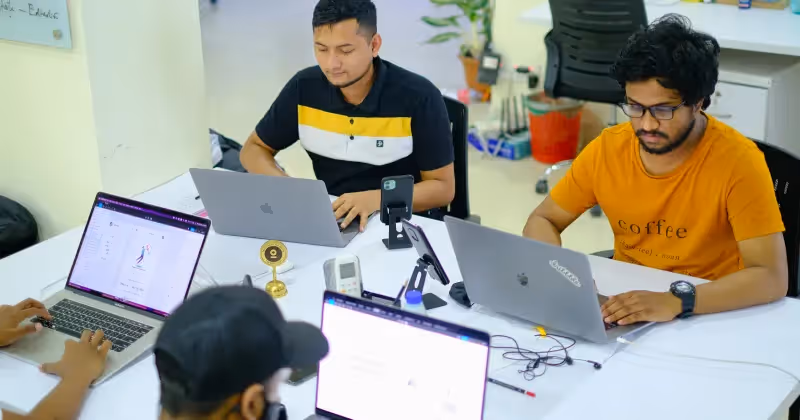 Four team members seated around a white office table collaborating and working on their laptops.