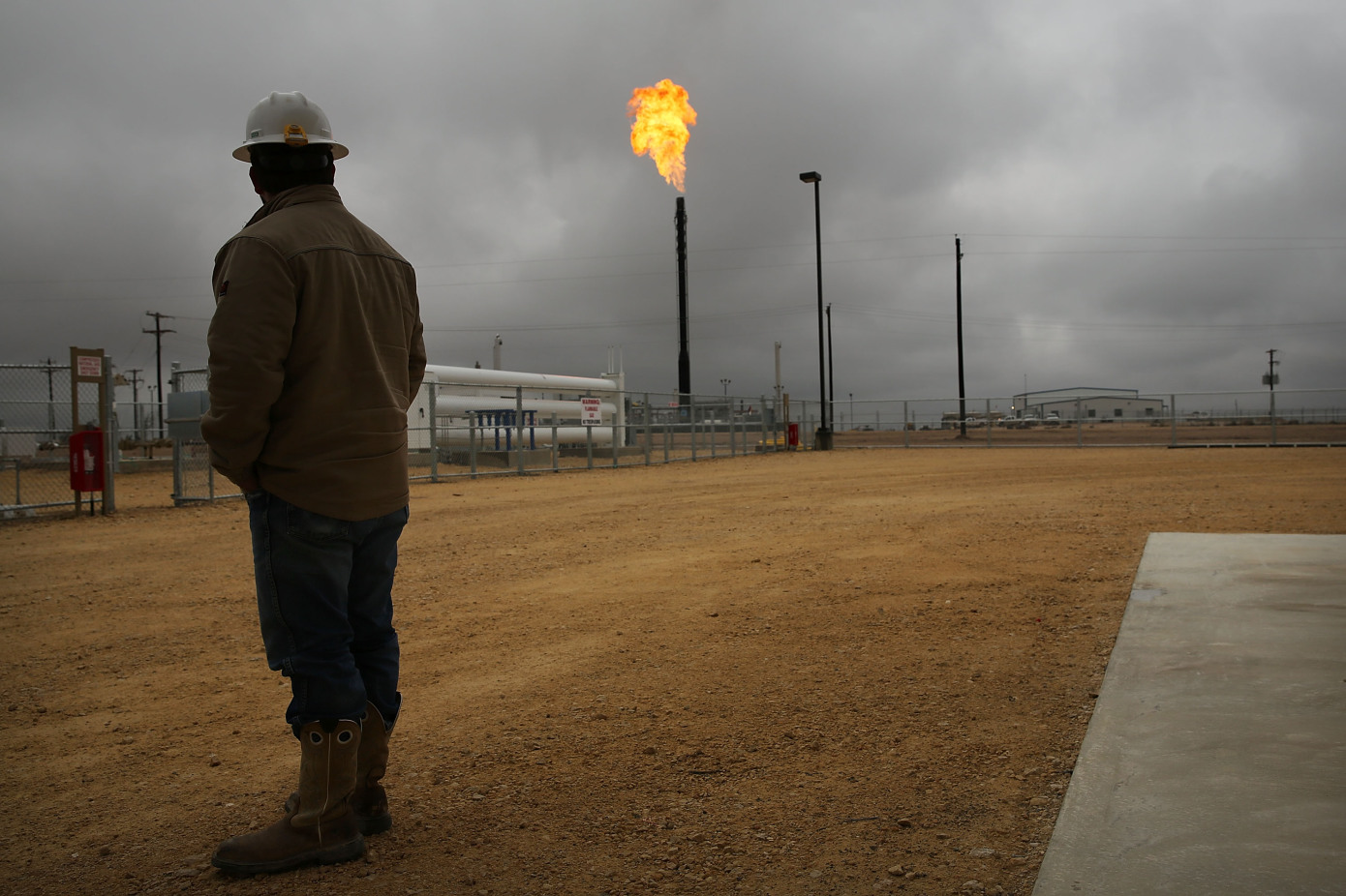 A worker in an industrial facility observes a flare stack emitting bright flames.