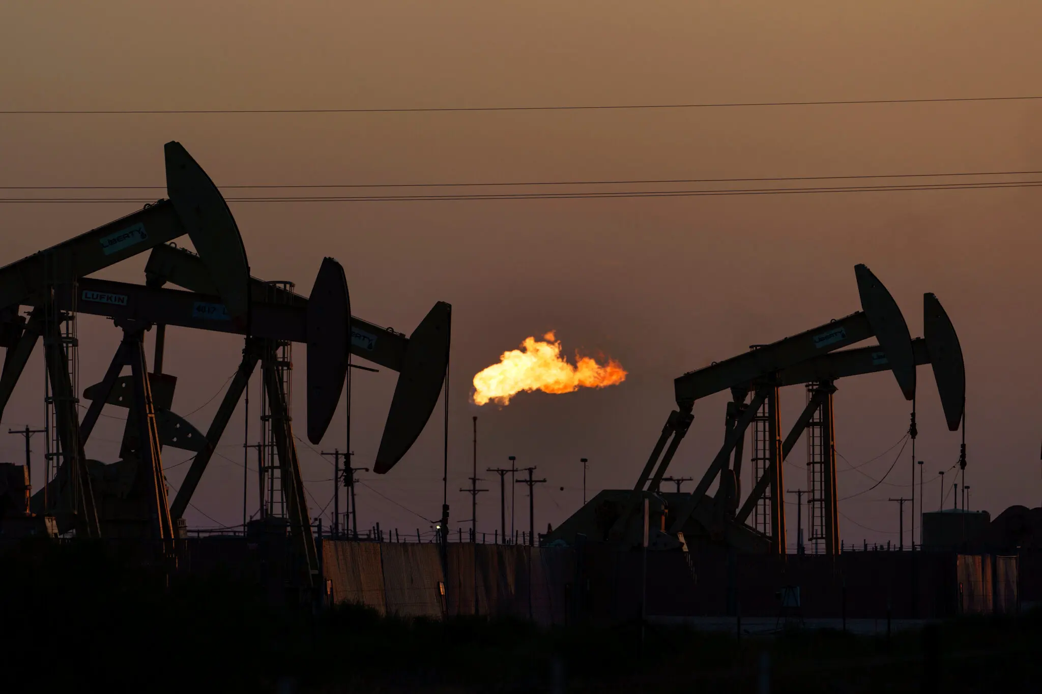 Oil pump jacks silhouetted against the evening sky flare gas burning in the background.