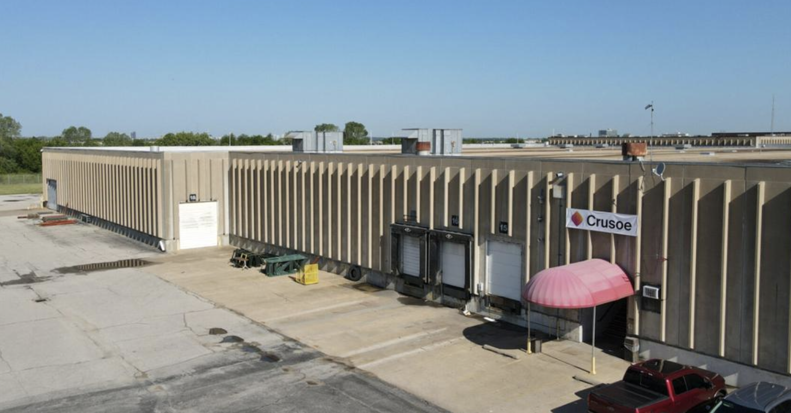 Exterior view of a Crusoe data center, a large industrial building with a prominent Crusoe sign.