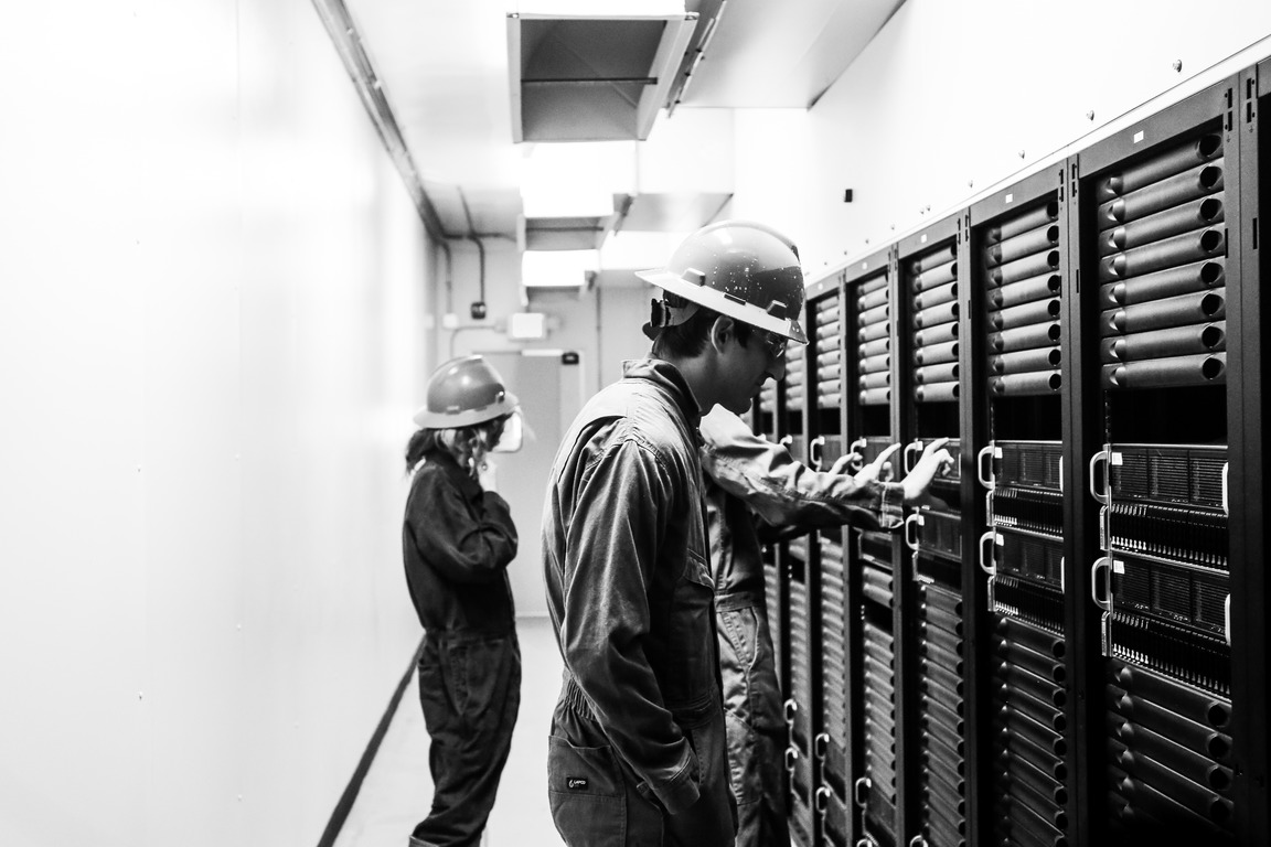 Three Crusoe employees wearing hard hats and protective gear inspect high-density GPU server racks in a Crusoe Cloud data center.
