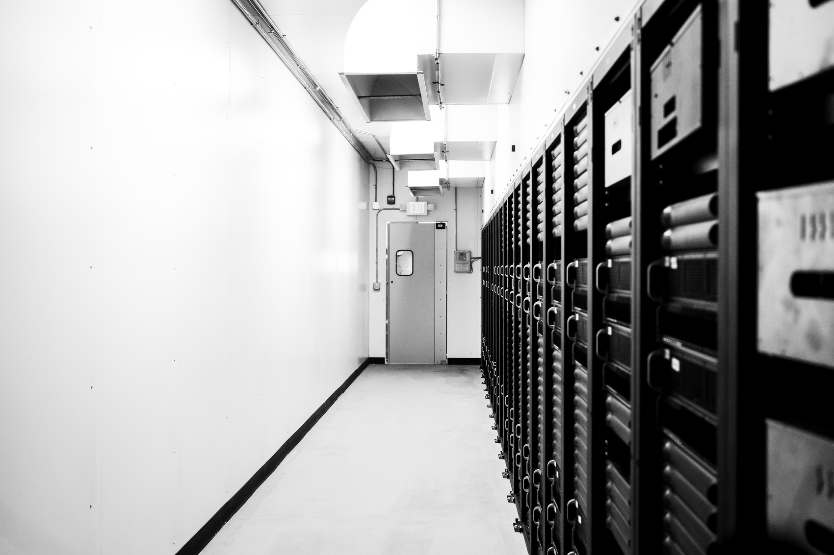 A black and white view down a long, narrow corridor in a data center.