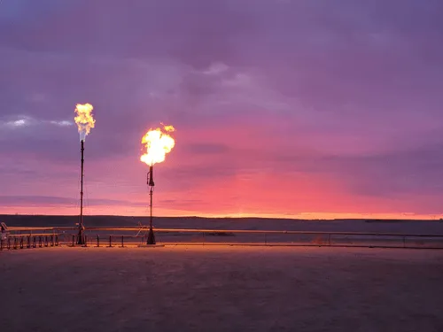 Sunset view featuring two flare stacks emitting flames against a vibrant purple and orange sky.