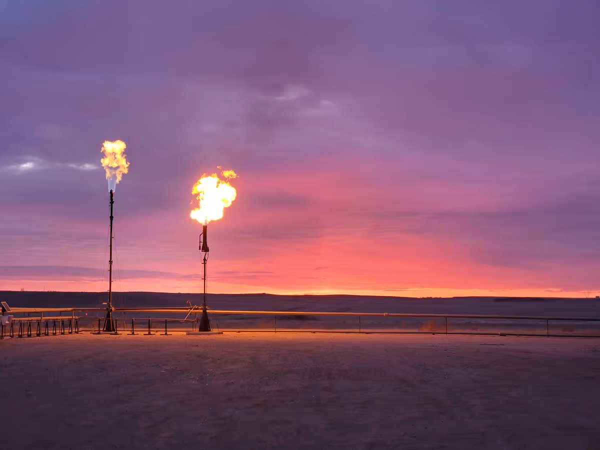 Sunset view featuring two flare stacks emitting flames against a vibrant purple and orange sky.