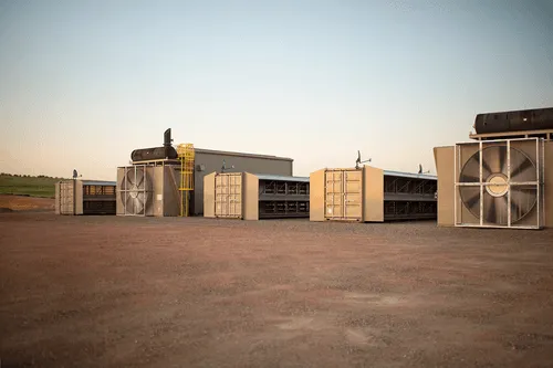 A series of modular data centers equipped with large cooling fans, operating at a remote industrial site.