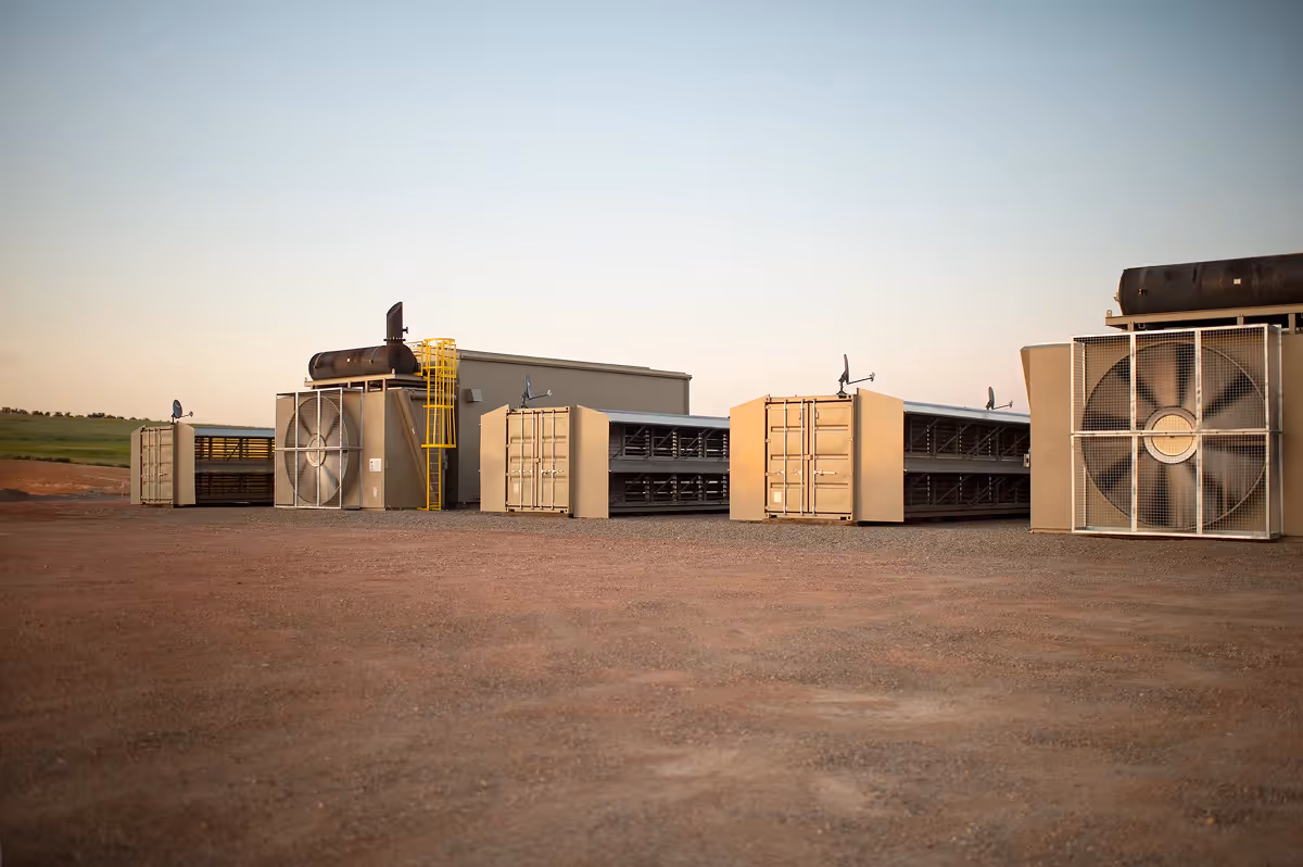 A series of modular data centers equipped with large cooling fans, operating at a remote industrial site.