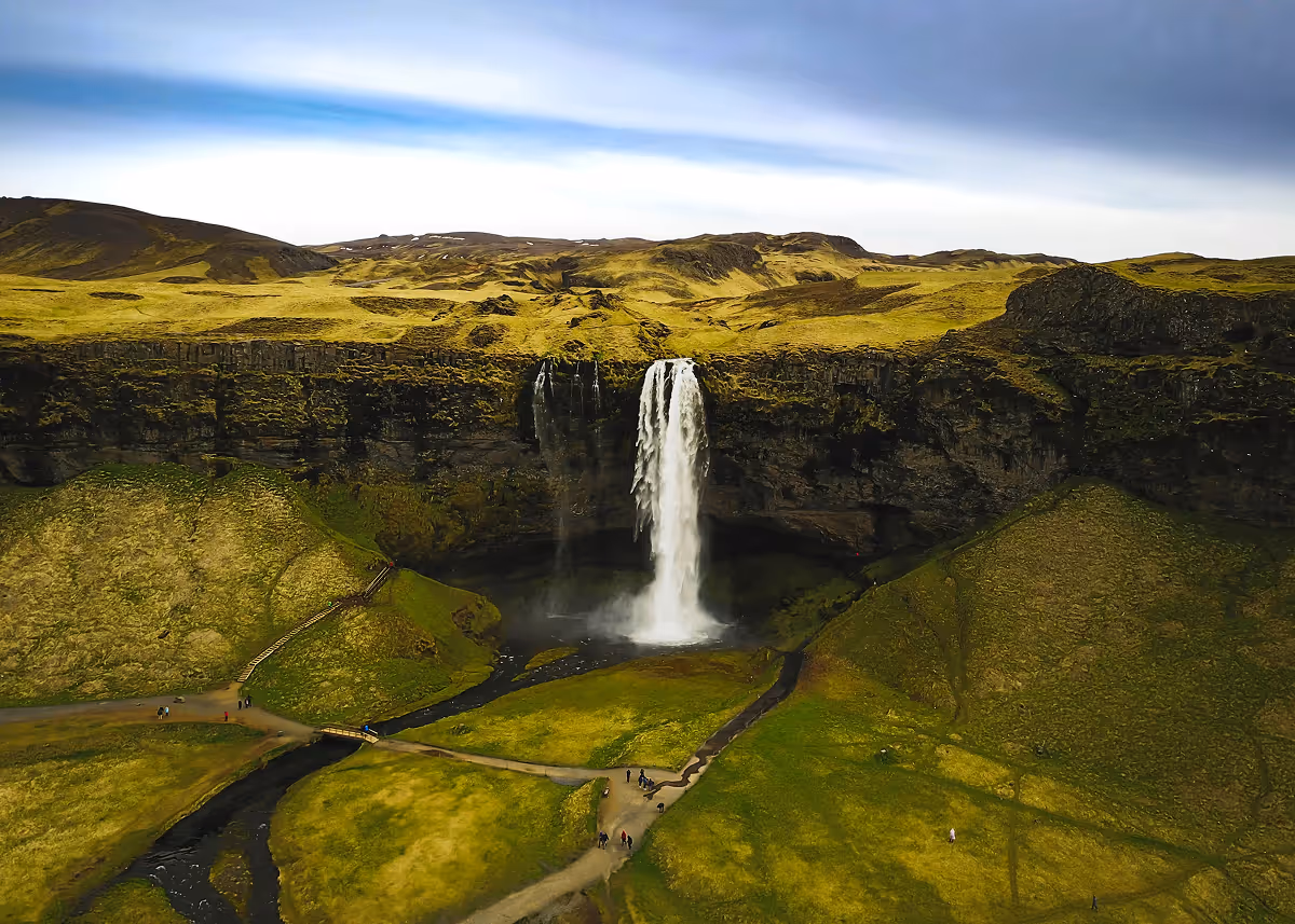 Aerial view of a waterfall plunging from a moss-covered cliff into a green valley.