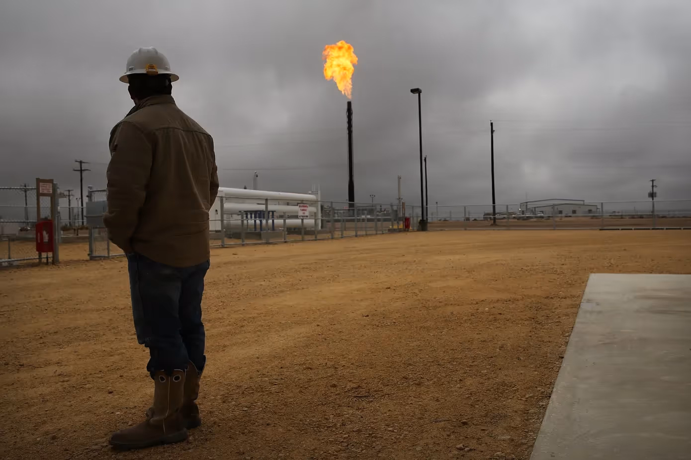 A worker in an industrial facility observes a flare stack emitting bright flames.