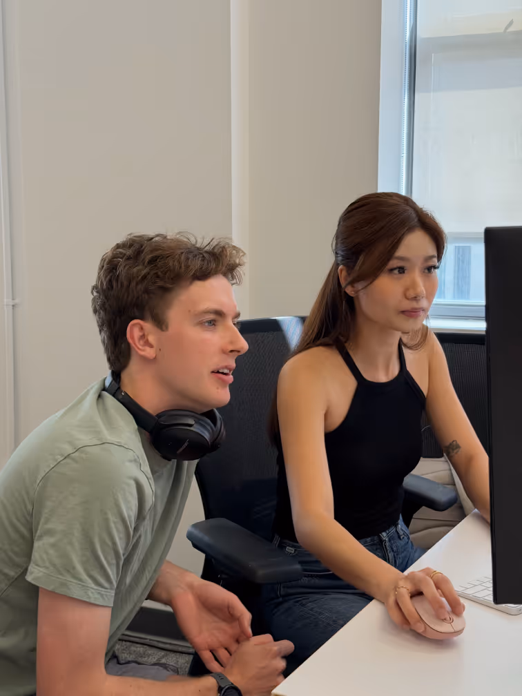 The picture of two colleagues using a computer in what's likely a work environment.