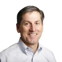 Smiling middle-aged man with short brown hair wearing a light gray checkered shirt.
