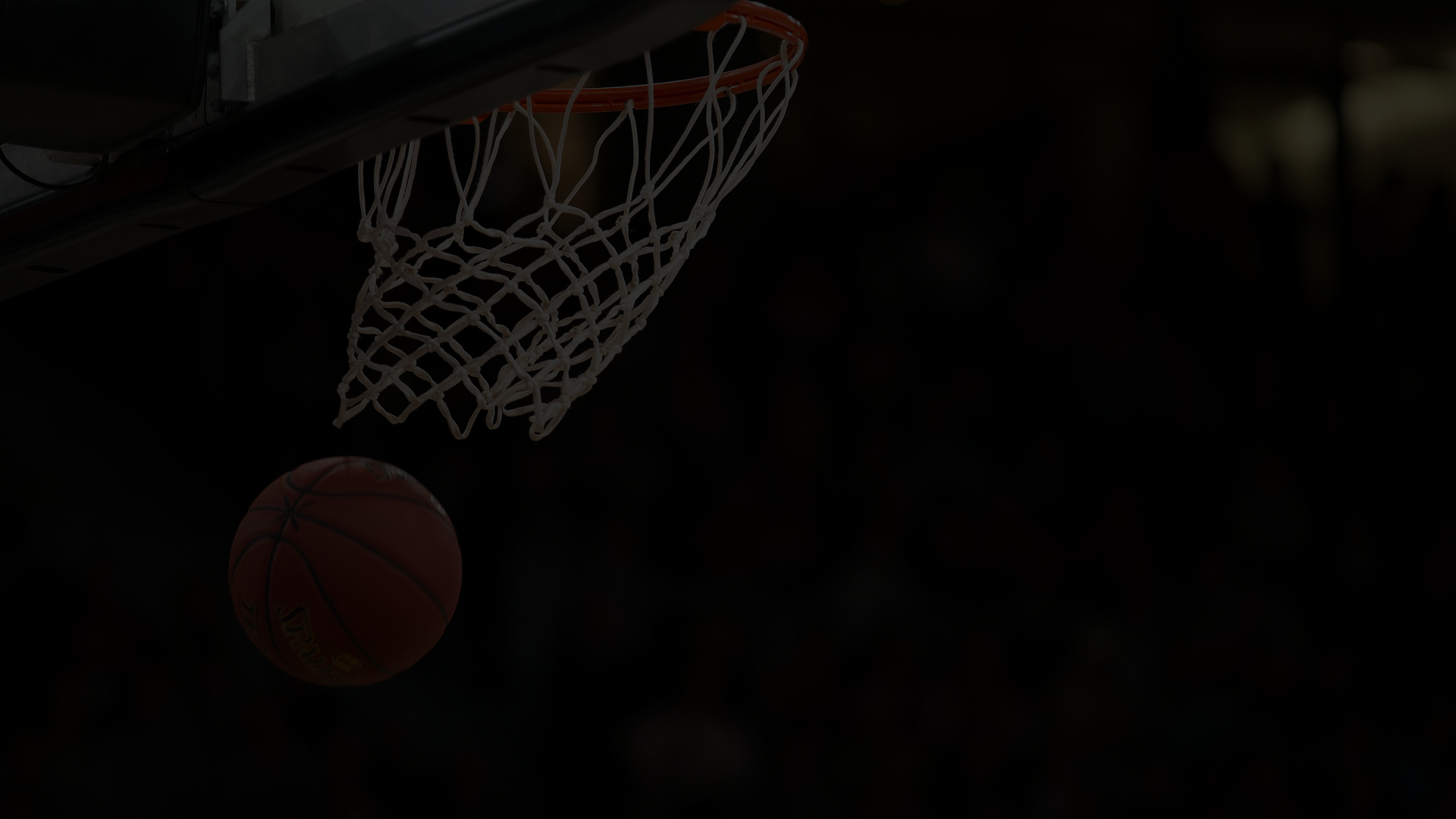 Un ballon de basket passe dans un filet de panier lors d'un match en salle.